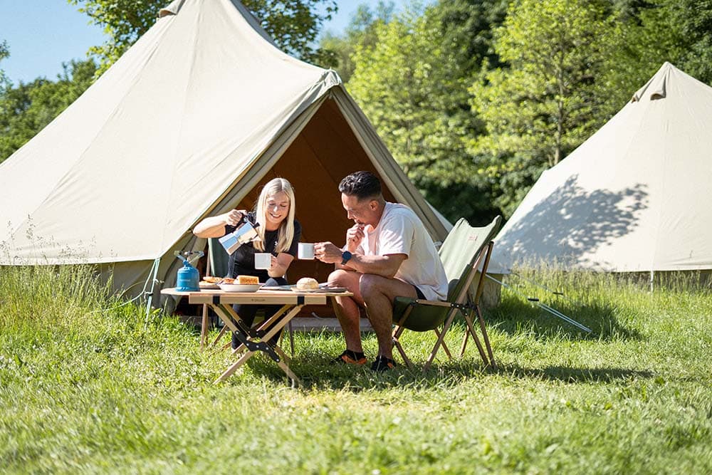 Everything you want to know about packrafting in the Eifel Germany Ardennes 3 a man and woman sitting at a table outside with tents Breakfast Glamping Eifel Germany