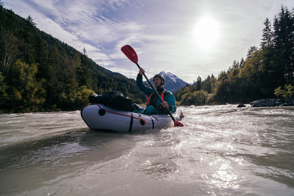 Packraft Trails for Beginners: Your Guide to the First Adventure 1 A serene view of a calm river surrounded by lush greenery, with a person in a packraft paddling under a clear blue sky. Ideal for showcasing beginner-friendly packraft trails in Europe.